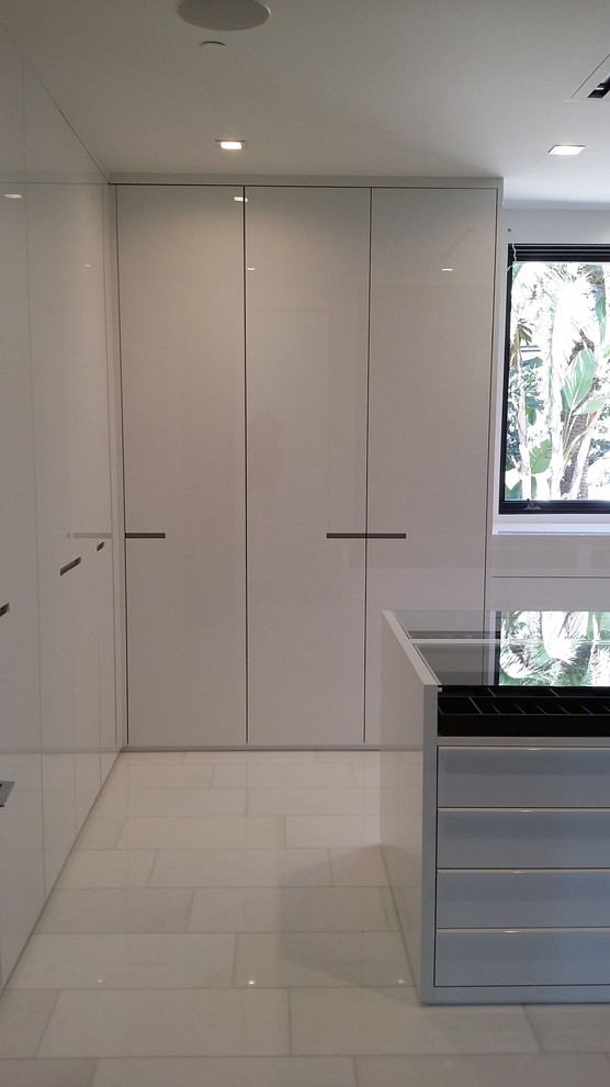 Large modern gender-neutral walk-in wardrobe in Los Angeles with flat-panel cabinets, white cabinets, marble floors and white floor.
