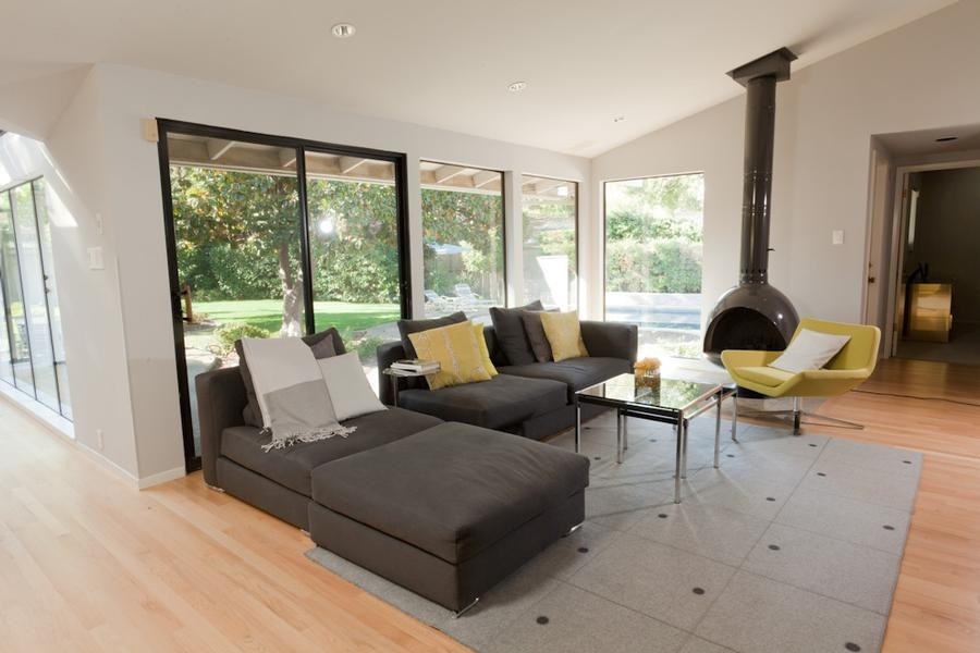 This is an example of a large contemporary open concept family room in Sacramento with grey walls, light hardwood floors and a hanging fireplace.