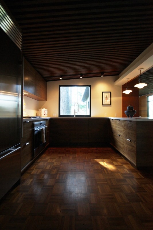 Photo of a mid-sized midcentury u-shaped eat-in kitchen in Portland with an undermount sink, flat-panel cabinets, dark wood cabinets, quartz benchtops, white splashback, stainless steel appliances, dark hardwood floors and no island.