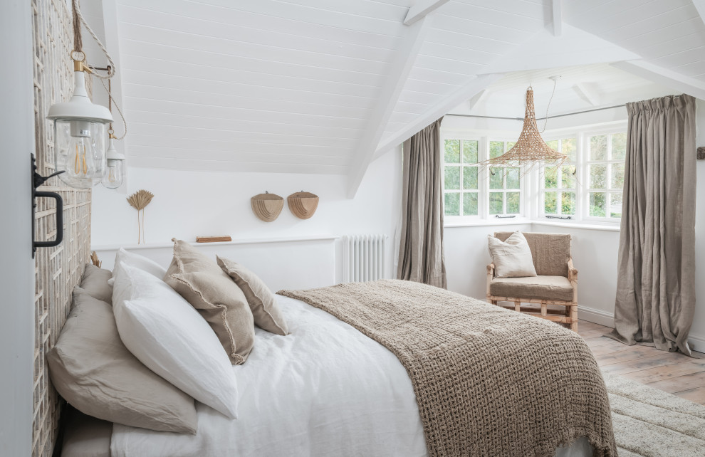 Mittelgroßes Maritimes Hauptschlafzimmer mit weißer Wandfarbe, braunem Holzboden, Kamin, beigem Boden und freigelegten Dachbalken in Cornwall