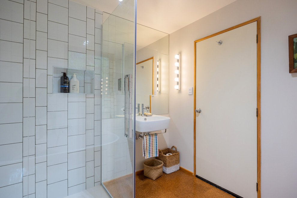Photo of a mid-sized eclectic bathroom in Auckland with a corner tub, a corner shower, white tile, ceramic tile, white walls, cork floors, a wall-mount sink, brown floor, a hinged shower door, a single vanity and a floating vanity.