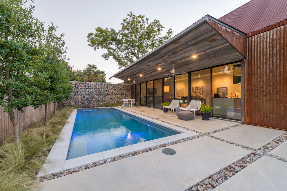 Small industrial backyard rectangular lap pool in Dallas with a water feature and concrete pavers.