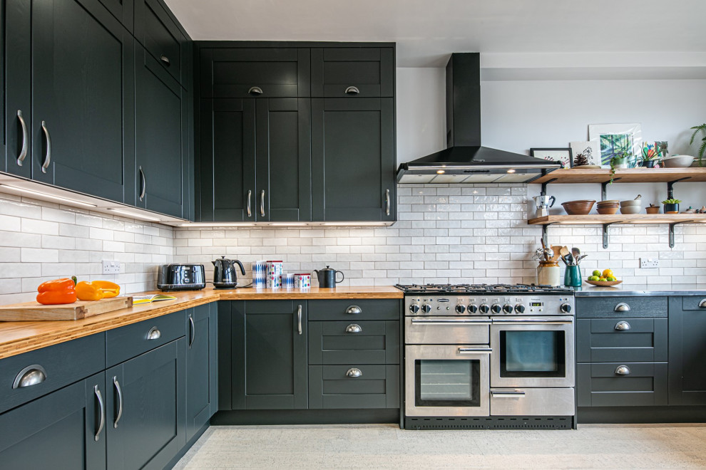Photo of a large industrial eat-in kitchen in Other with shaker cabinets, blue cabinets, stainless steel benchtops, white splashback, subway tile splashback, stainless steel appliances, cork floors, a peninsula and white floor.