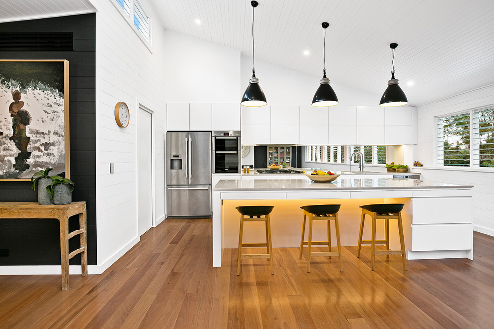 This is an example of a contemporary l-shaped open plan kitchen in Sydney with a drop-in sink, flat-panel cabinets, white cabinets, mirror splashback, stainless steel appliances, medium hardwood floors and with island.