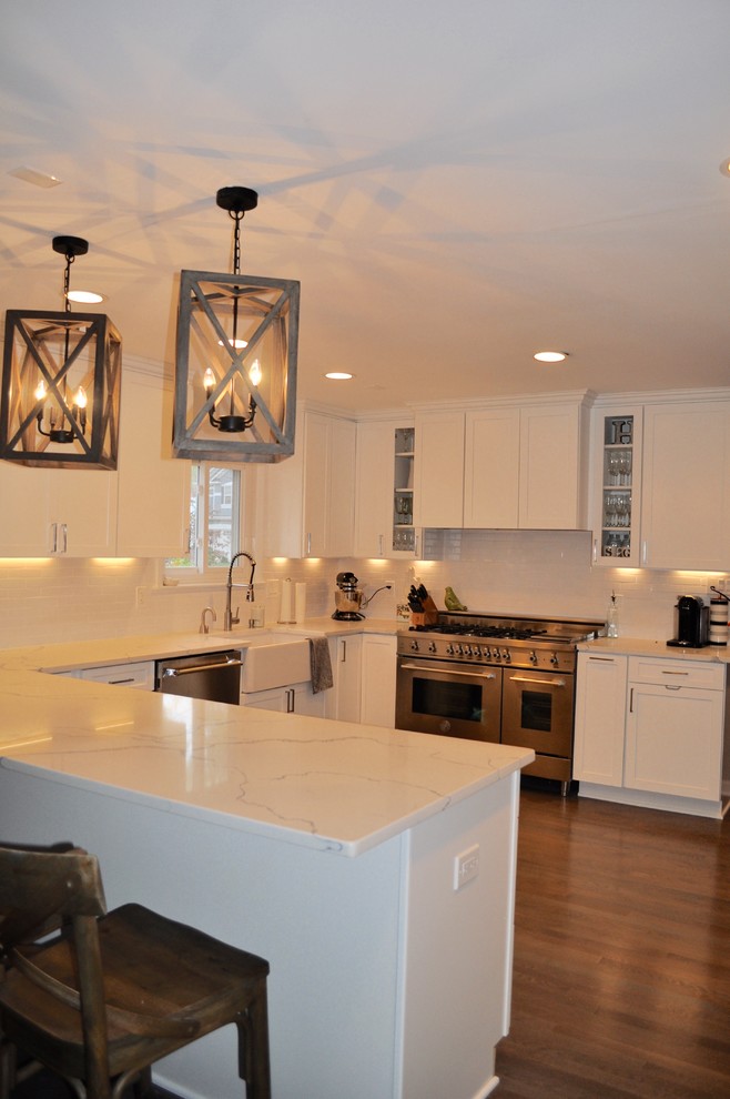 Mid-sized transitional u-shaped dark wood floor and brown floor kitchen photo in DC Metro with a farmhouse sink, shaker cabinets, white cabinets, marble countertops, white backsplash, subway tile backsplash, stainless steel appliances and a peninsula