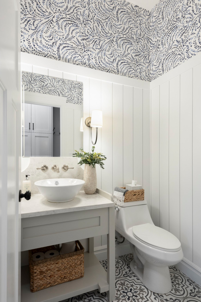 This is an example of a mid-sized traditional powder room with shaker cabinets, grey cabinets, white walls, porcelain floors, a vessel sink, engineered quartz benchtops, multi-coloured floor, white benchtops, a freestanding vanity and wallpaper.