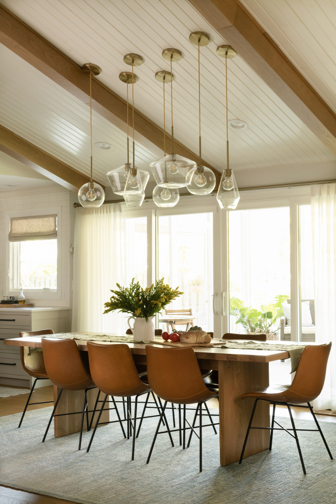Cette photo montre une grande salle à manger ouverte sur la cuisine rétro avec un mur blanc, un sol en bois brun, poutres apparentes, un plafond en lambris de bois, un plafond voûté et un sol marron.