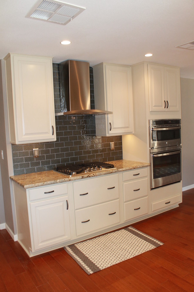 Mid-sized transitional u-shaped dark wood floor and brown floor eat-in kitchen photo in Phoenix with an undermount sink, raised-panel cabinets, white cabinets, granite countertops, green backsplash, glass tile backsplash, stainless steel appliances and a peninsula