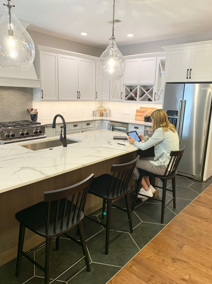 Photo of a large transitional l-shaped eat-in kitchen in Other with a farmhouse sink, recessed-panel cabinets, white cabinets, quartz benchtops, multi-coloured splashback, ceramic splashback, stainless steel appliances, ceramic floors, with island, black floor and white benchtop.