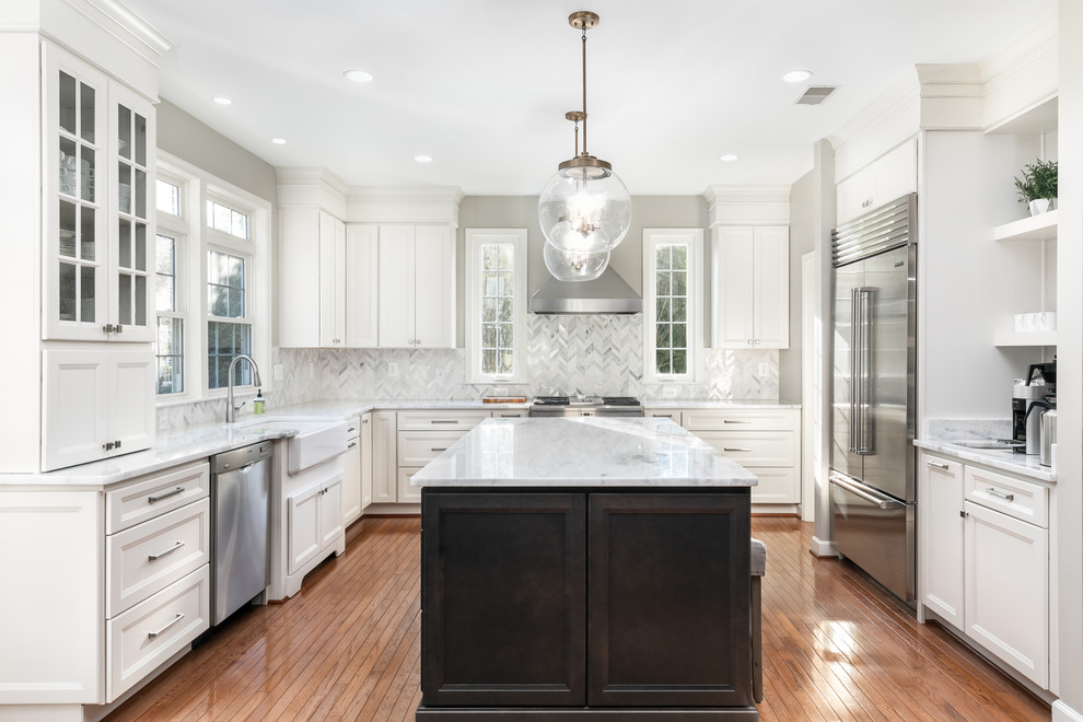Photo of a large transitional u-shaped eat-in kitchen in DC Metro with a farmhouse sink, recessed-panel cabinets, white cabinets, quartzite benchtops, white splashback, stainless steel appliances, medium hardwood floors, with island, brown floor, white benchtop and mosaic tile splashback.