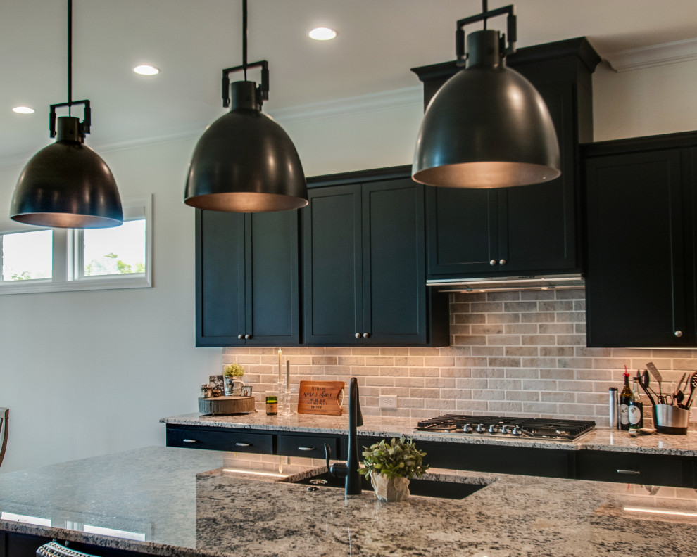 This is an example of a mid-sized transitional eat-in kitchen in Nashville with an undermount sink, shaker cabinets, black cabinets, granite benchtops, grey splashback, limestone splashback, stainless steel appliances, medium hardwood floors, with island, brown floor and multi-coloured benchtop.