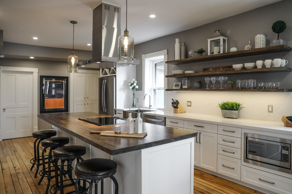 Eat-in kitchen - mid-sized transitional single-wall medium tone wood floor and brown floor eat-in kitchen idea with a farmhouse sink, shaker cabinets, white cabinets, white backsplash, stainless steel appliances, an island and white countertops