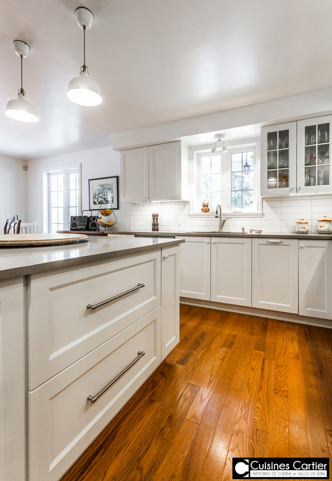 Inspiration for a large transitional medium tone wood floor eat-in kitchen remodel in Montreal with a double-bowl sink, shaker cabinets, white cabinets, quartzite countertops, white backsplash, ceramic backsplash, stainless steel appliances and an island