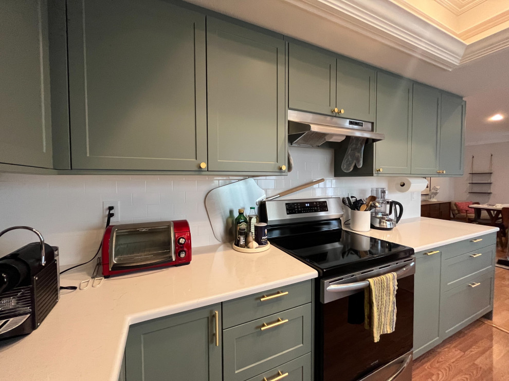 Photo of a mid-sized transitional u-shaped eat-in kitchen in Orange County with an undermount sink, shaker cabinets, green cabinets, yellow splashback, subway tile splashback, stainless steel appliances, medium hardwood floors, a peninsula, brown floor, white benchtop and recessed.