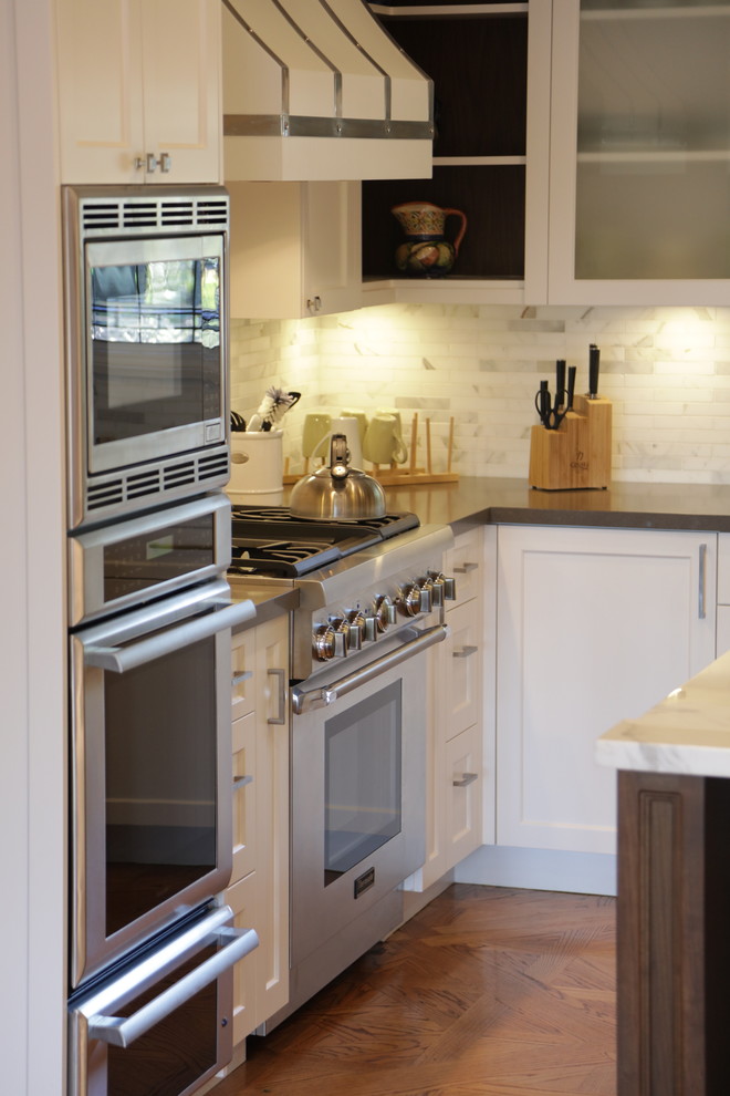 Example of a large transitional u-shaped medium tone wood floor eat-in kitchen design in Los Angeles with an undermount sink, recessed-panel cabinets, white cabinets, wood countertops, white backsplash, stone tile backsplash, stainless steel appliances and an island