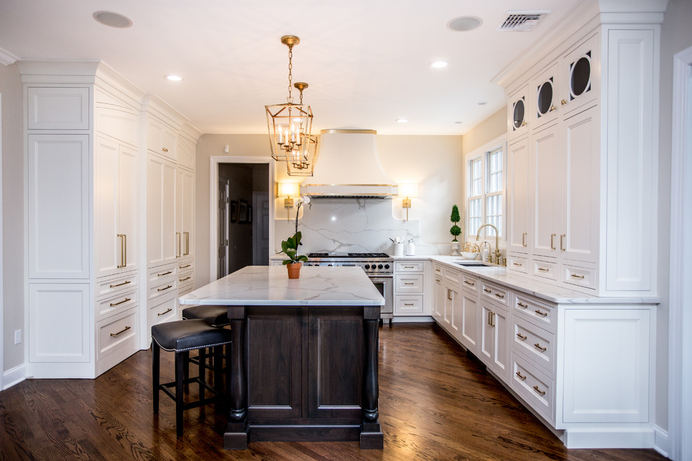 Design ideas for a large transitional l-shaped eat-in kitchen with an undermount sink, recessed-panel cabinets, white cabinets, marble benchtops, white splashback, marble splashback, panelled appliances, dark hardwood floors, with island and brown floor.