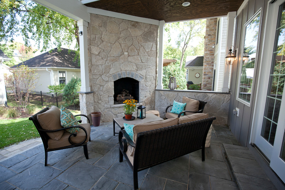 This is an example of a mid-sized country backyard patio in Chicago with a fire feature, natural stone pavers and a roof extension.