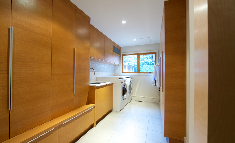 Inspiration for a large contemporary galley dedicated laundry room in Vancouver with an undermount sink, flat-panel cabinets, medium wood cabinets, white walls, a side-by-side washer and dryer, quartz benchtops, porcelain floors and white floor.