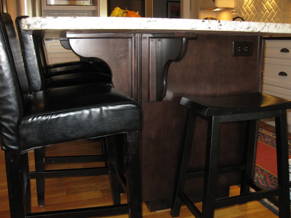 Inspiration for a transitional l-shaped medium tone wood floor eat-in kitchen remodel in Boston with an undermount sink, shaker cabinets, white cabinets, granite countertops, white backsplash, ceramic backsplash, stainless steel appliances, an island and black countertops