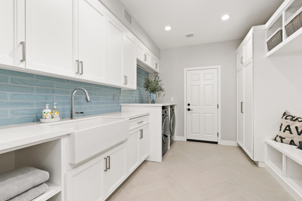 This is an example of a large beach style galley dedicated laundry room in San Diego with a farmhouse sink, shaker cabinets, white cabinets, quartz benchtops, blue splashback, ceramic splashback, grey walls, porcelain floors, a side-by-side washer and dryer, grey floor and white benchtop.