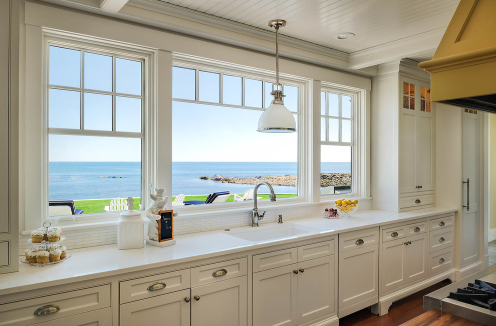 Design ideas for a mid-sized beach style u-shaped eat-in kitchen in Portland Maine with an undermount sink, shaker cabinets, white cabinets, marble benchtops, white splashback, porcelain splashback, stainless steel appliances, medium hardwood floors and with island.