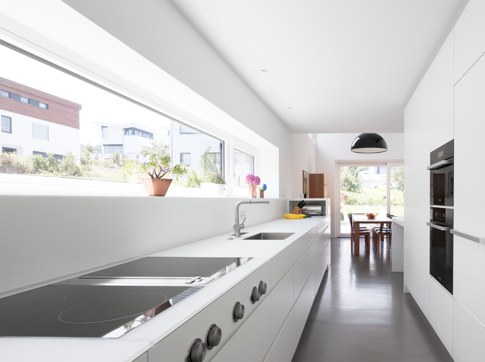 Photo of a mid-sized contemporary galley separate kitchen in Stuttgart with an undermount sink, flat-panel cabinets, white cabinets, panelled appliances, white splashback and no island.