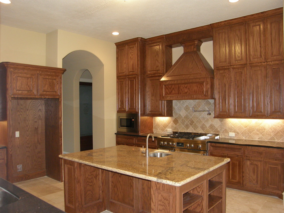 Inspiration for a large traditional l-shaped open plan kitchen in Houston with an undermount sink, raised-panel cabinets, dark wood cabinets, granite benchtops, stone tile splashback, stainless steel appliances, travertine floors and with island.