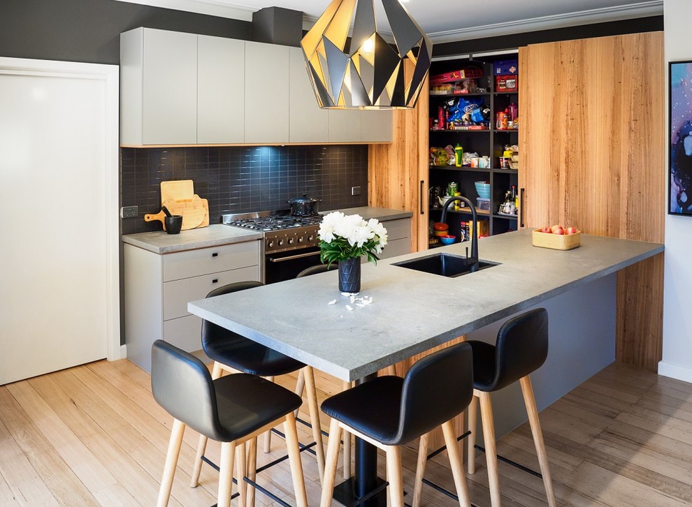 Small contemporary u-shaped eat-in kitchen in Melbourne with a single-bowl sink, flat-panel cabinets, light wood cabinets, quartzite benchtops, black splashback, ceramic splashback, stainless steel appliances, light hardwood floors, with island and beige floor.