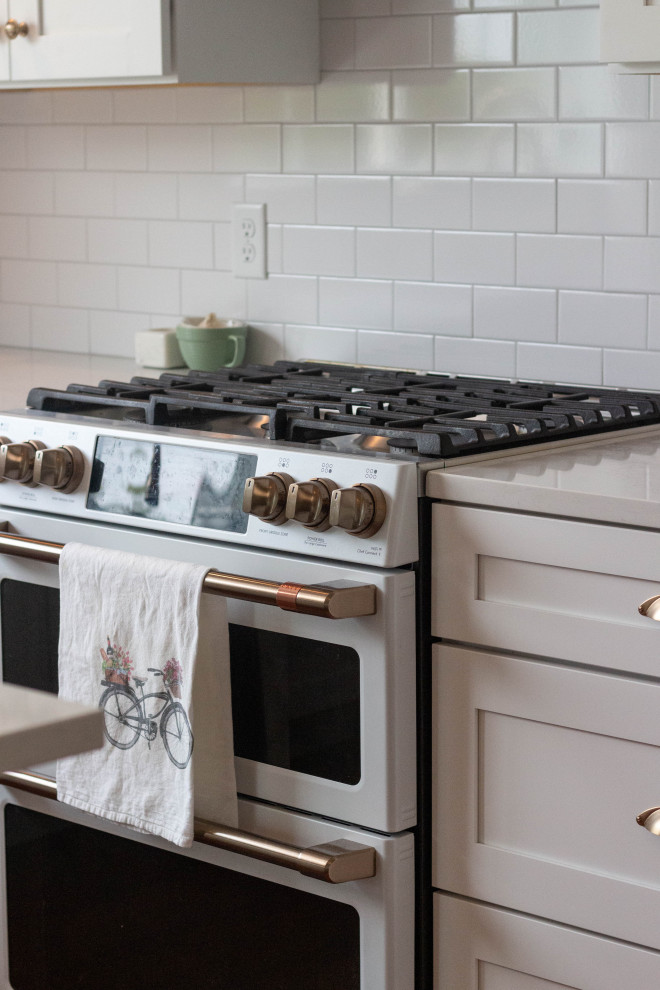 Example of a mid-sized transitional l-shaped medium tone wood floor and brown floor open concept kitchen design with an undermount sink, shaker cabinets, white cabinets, quartzite countertops, white backsplash, ceramic backsplash, white appliances, an island and white countertops