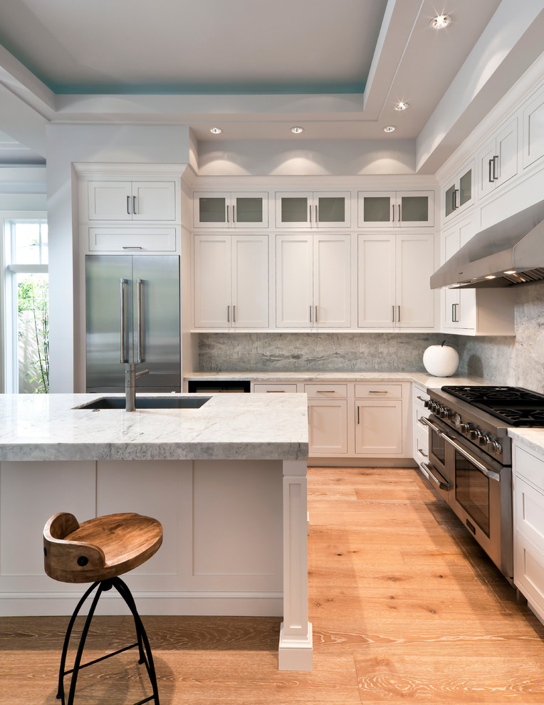 Example of a large transitional l-shaped light wood floor and tray ceiling open concept kitchen design in Miami with an undermount sink, shaker cabinets, white cabinets, quartz countertops, gray backsplash, quartz backsplash, stainless steel appliances, an island and gray countertops
