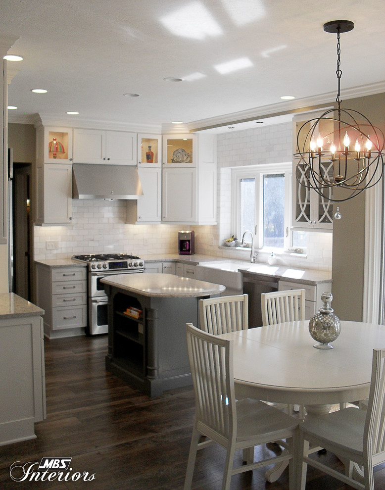 Mid-sized transitional u-shaped medium tone wood floor eat-in kitchen photo with a farmhouse sink, shaker cabinets, white cabinets, quartzite countertops, white backsplash, subway tile backsplash, stainless steel appliances and an island
