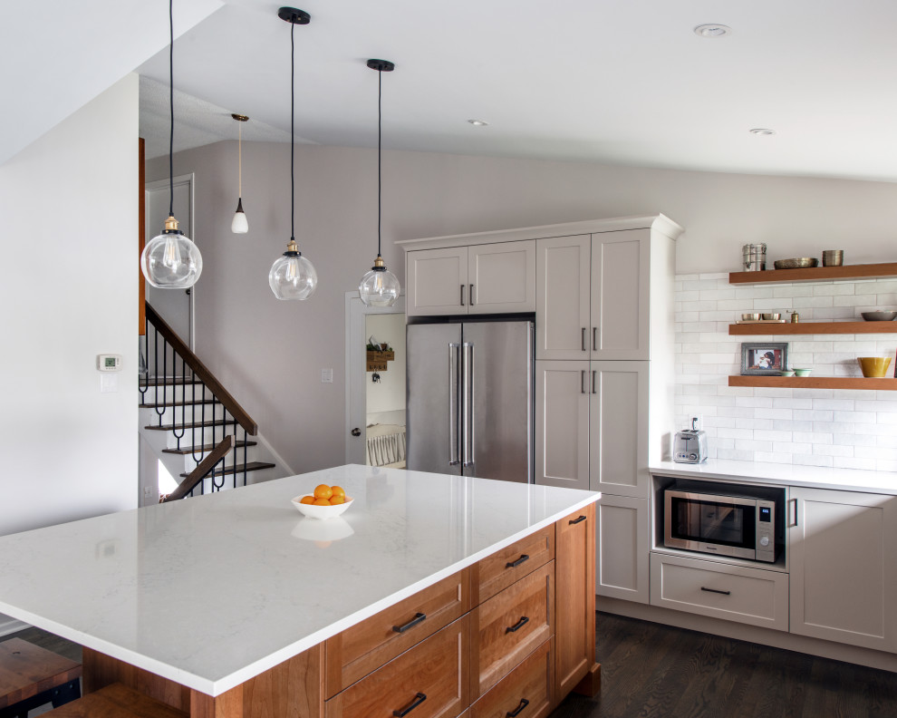 Example of a mid-sized transitional l-shaped medium tone wood floor, gray floor and vaulted ceiling open concept kitchen design in Ottawa with a double-bowl sink, shaker cabinets, gray cabinets, quartz countertops, white backsplash, subway tile backsplash, stainless steel appliances, an island and white countertops