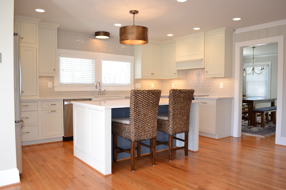 Inspiration for a mid-sized transitional u-shaped light wood floor and brown floor open concept kitchen remodel with a farmhouse sink, recessed-panel cabinets, white cabinets, quartz countertops, beige backsplash, ceramic backsplash, stainless steel appliances and an island