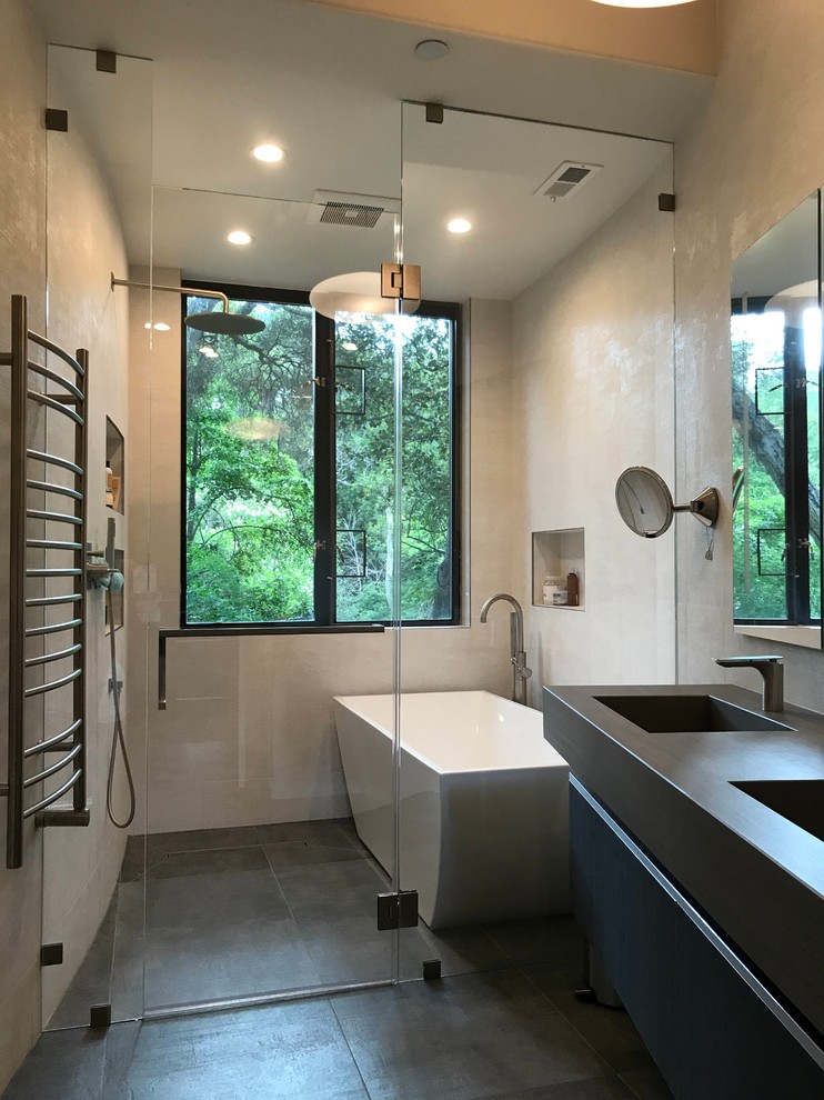 Photo of a contemporary wet room bathroom in San Francisco with flat-panel cabinets, black cabinets, a freestanding tub, beige tile, beige walls, an integrated sink, a hinged shower door, grey benchtops, porcelain floors and grey floor.