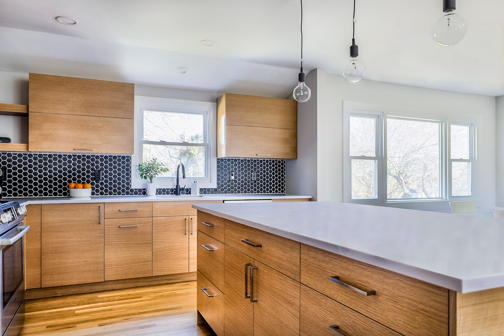 This is an example of a mid-sized contemporary l-shaped eat-in kitchen in New York with an undermount sink, flat-panel cabinets, light wood cabinets, quartzite benchtops, black splashback, porcelain splashback, stainless steel appliances, light hardwood floors, with island and white benchtop.