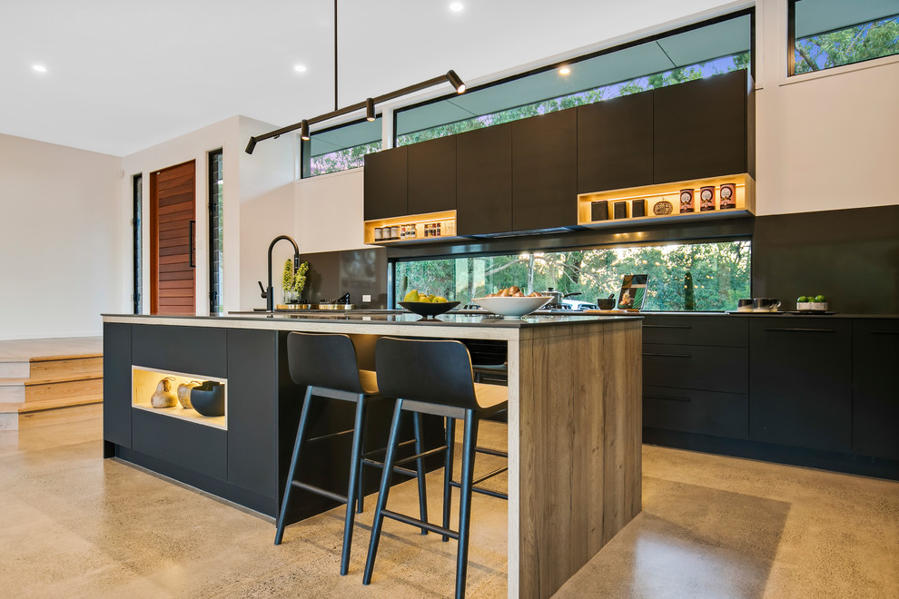 Photo of a contemporary galley open plan kitchen in Sunshine Coast with flat-panel cabinets, black cabinets, window splashback, panelled appliances, concrete floors, with island, beige floor and black benchtop.