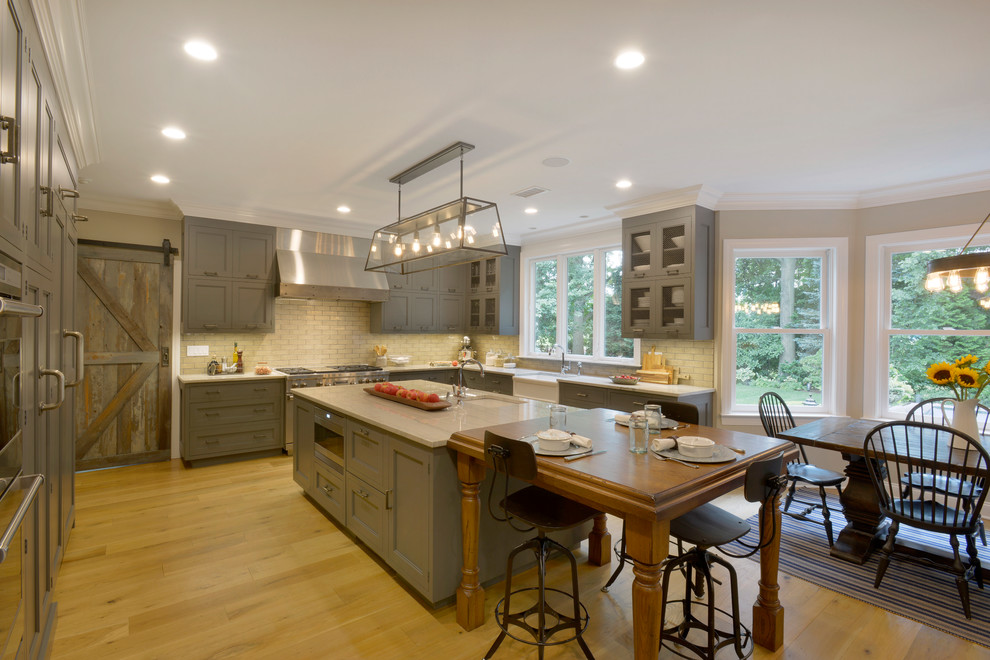 Inspiration for an expansive traditional u-shaped eat-in kitchen in New York with a farmhouse sink, recessed-panel cabinets, grey cabinets, quartzite benchtops, beige splashback, brick splashback, stainless steel appliances, light hardwood floors, with island, beige floor and multi-coloured benchtop.