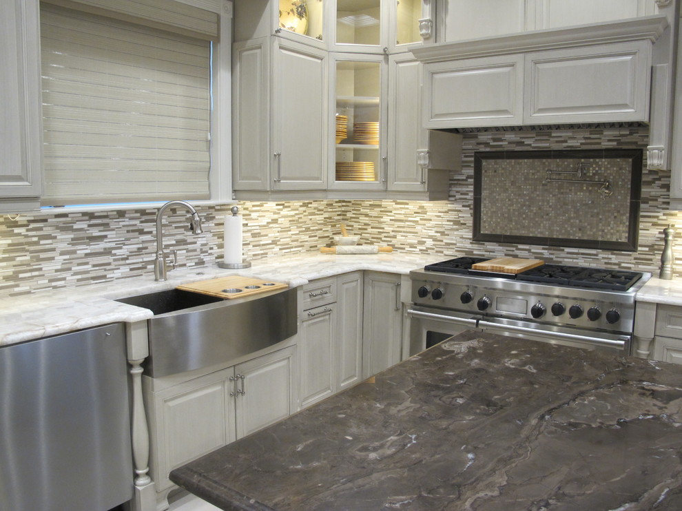 Photo of a mid-sized transitional u-shaped kitchen in New Orleans with quartzite benchtops, grey splashback, stone tile splashback, stainless steel appliances, porcelain floors, a farmhouse sink, raised-panel cabinets, beige cabinets and with island.