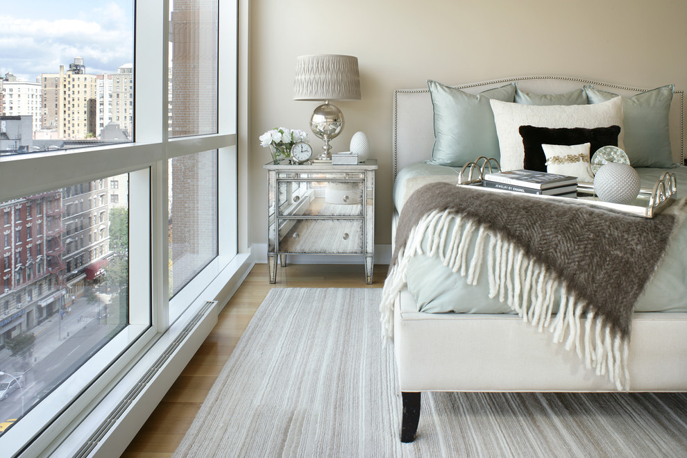 This is an example of a transitional master bedroom in New York with beige walls and light hardwood floors.