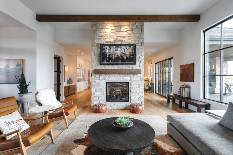 This is an example of a medium sized open plan games room in Calgary with dark hardwood flooring, a two-sided fireplace, a stacked stone fireplace surround, a wall mounted tv and exposed beams.