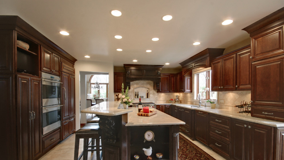Mid-sized transitional u-shaped eat-in kitchen photo with an undermount sink, raised-panel cabinets, dark wood cabinets, beige backsplash, stainless steel appliances and an island