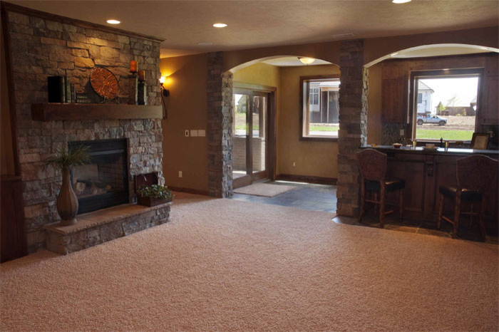 Design ideas for a mid-sized contemporary basement in Wichita with beige walls, carpet, a two-sided fireplace, a stone fireplace surround and beige floor.
