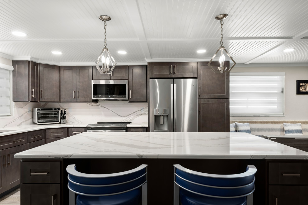 Inredning av ett maritimt mellanstort vit vitt kök, med en undermonterad diskho, skåp i shakerstil, skåp i mörkt trä, bänkskiva i kvarts, vitt stänkskydd, rostfria vitvaror, vinylgolv, en köksö och beiget golv