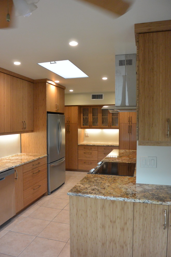 Example of a transitional u-shaped porcelain tile and beige floor eat-in kitchen design with an undermount sink, flat-panel cabinets, light wood cabinets, granite countertops, stainless steel appliances, a peninsula and brown countertops