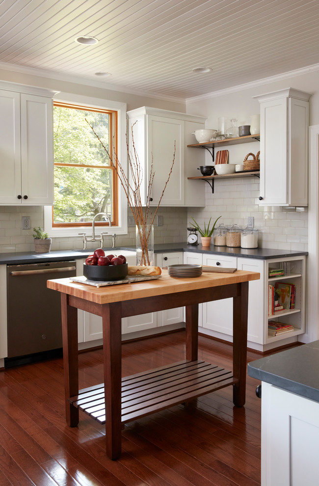 Design ideas for a country l-shaped kitchen in Baltimore with a farmhouse sink, shaker cabinets, white cabinets, white splashback, subway tile splashback, stainless steel appliances, dark hardwood floors, with island, grey benchtop and soapstone benchtops.