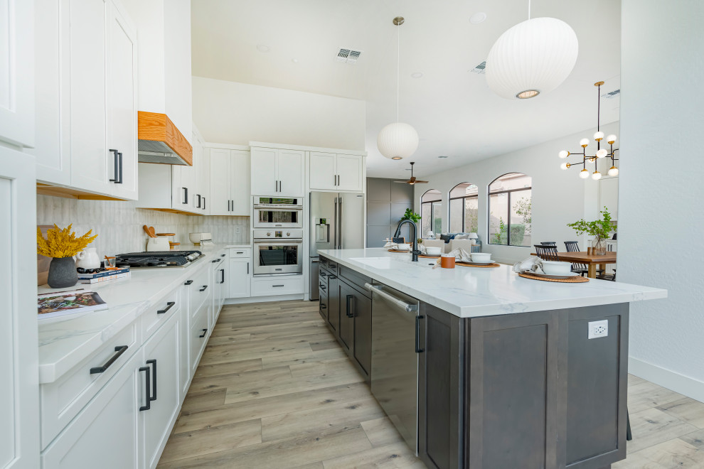 This is an example of a transitional kitchen in Phoenix with a single-bowl sink, shaker cabinets, white cabinets, quartz benchtops, white splashback, subway tile splashback, stainless steel appliances, vinyl floors, with island, brown floor and white benchtop.