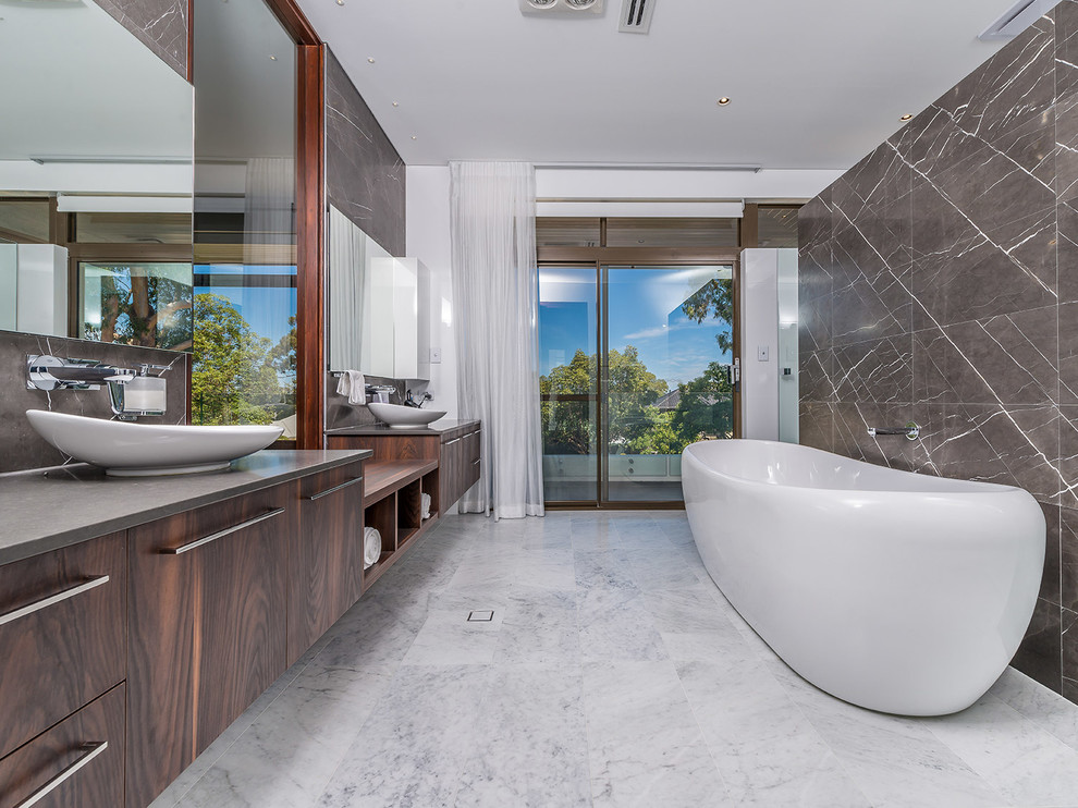 Photo of a contemporary master bathroom in Perth with flat-panel cabinets, dark wood cabinets, a freestanding tub, brown tile, marble floors, a vessel sink, brown walls and grey benchtops.