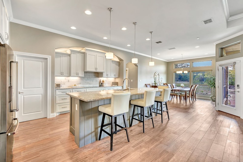 Mid-sized traditional single-wall open plan kitchen in Austin with an undermount sink, shaker cabinets, grey cabinets, granite benchtops, grey splashback, marble splashback, stainless steel appliances, dark hardwood floors, with island and brown floor.