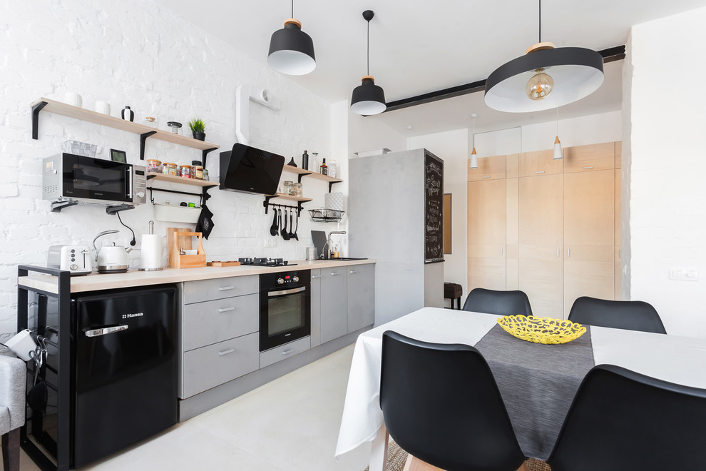 Mid-sized industrial single-wall eat-in kitchen in Other with a drop-in sink, grey cabinets, wood benchtops, white splashback, black appliances, plywood floors, no island, beige floor and flat-panel cabinets.