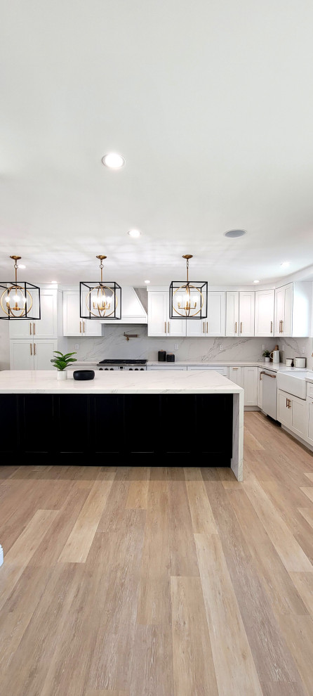 This is an example of a large modern l-shaped open plan kitchen in Los Angeles with a farmhouse sink, shaker cabinets, white cabinets, quartz benchtops, white splashback, engineered quartz splashback, white appliances, vinyl floors, with island, brown floor and white benchtop.
